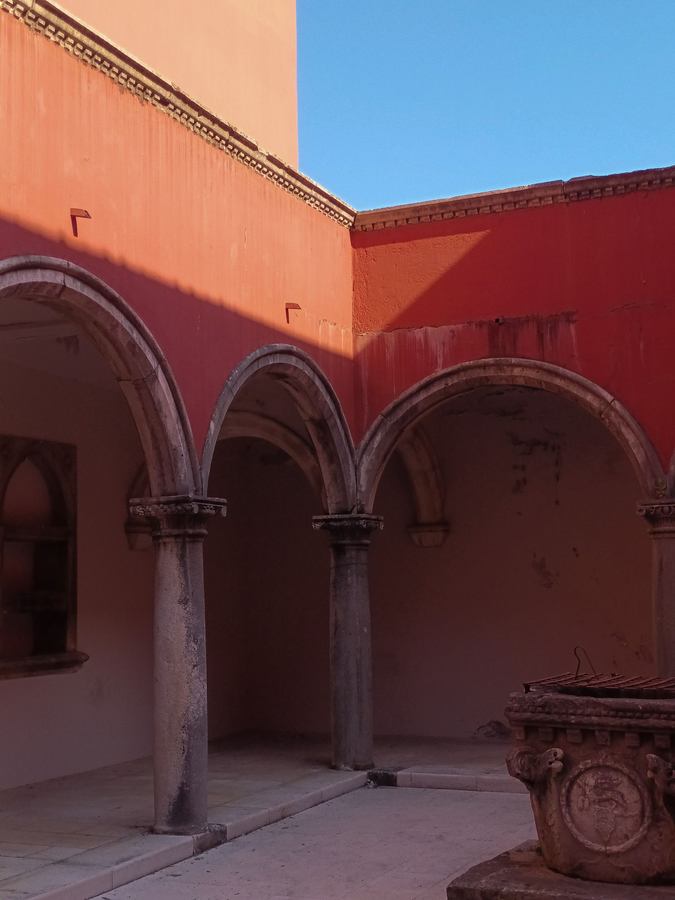 Sunlit historic courtyard framed by red arches